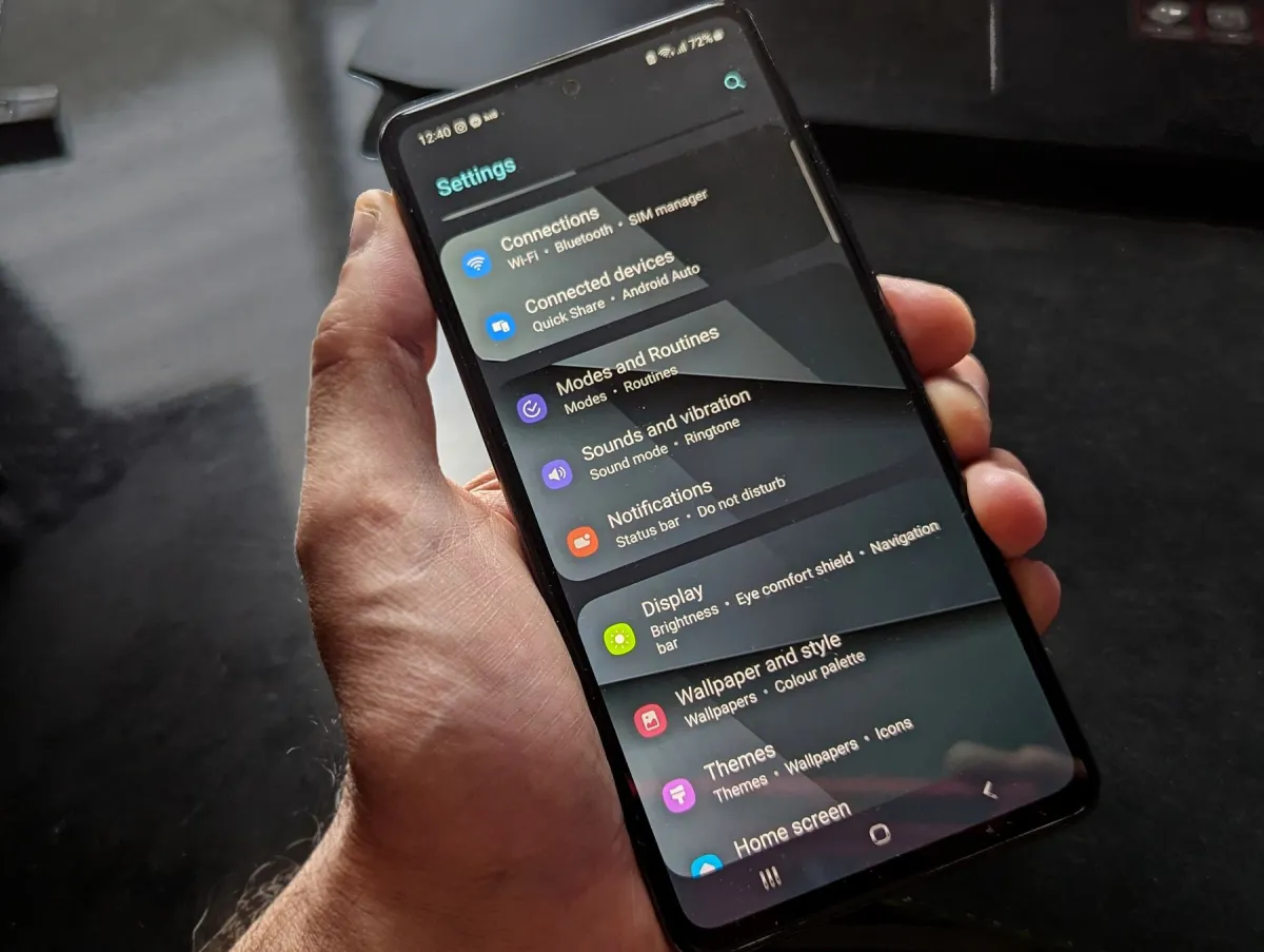 A hand holding a smartphone displaying its settings menu.