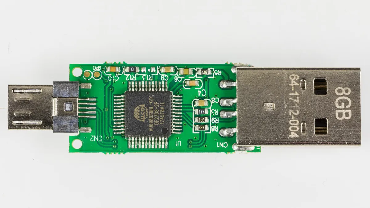 Macro photograph of an exposed green USB flash-drive circuit board with metal plugs at each end.