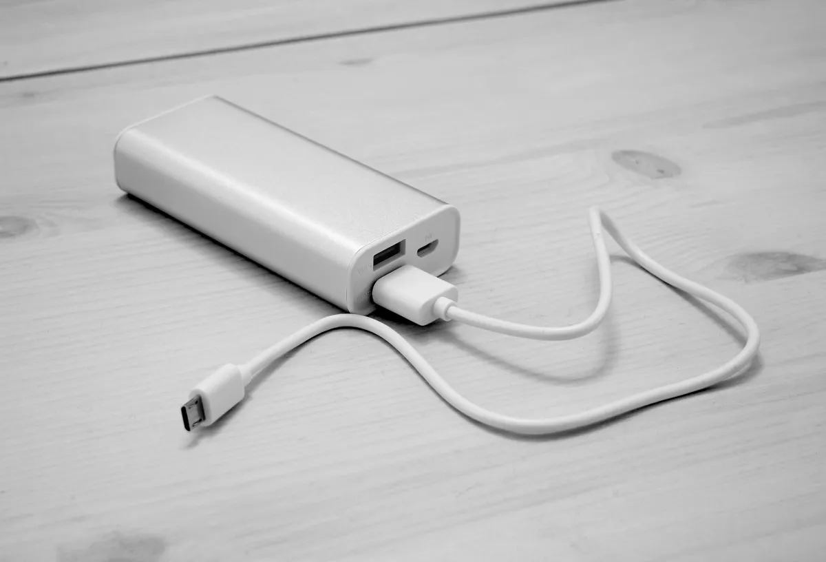 Silver power bank with a white cable connected, resting on a wooden table.