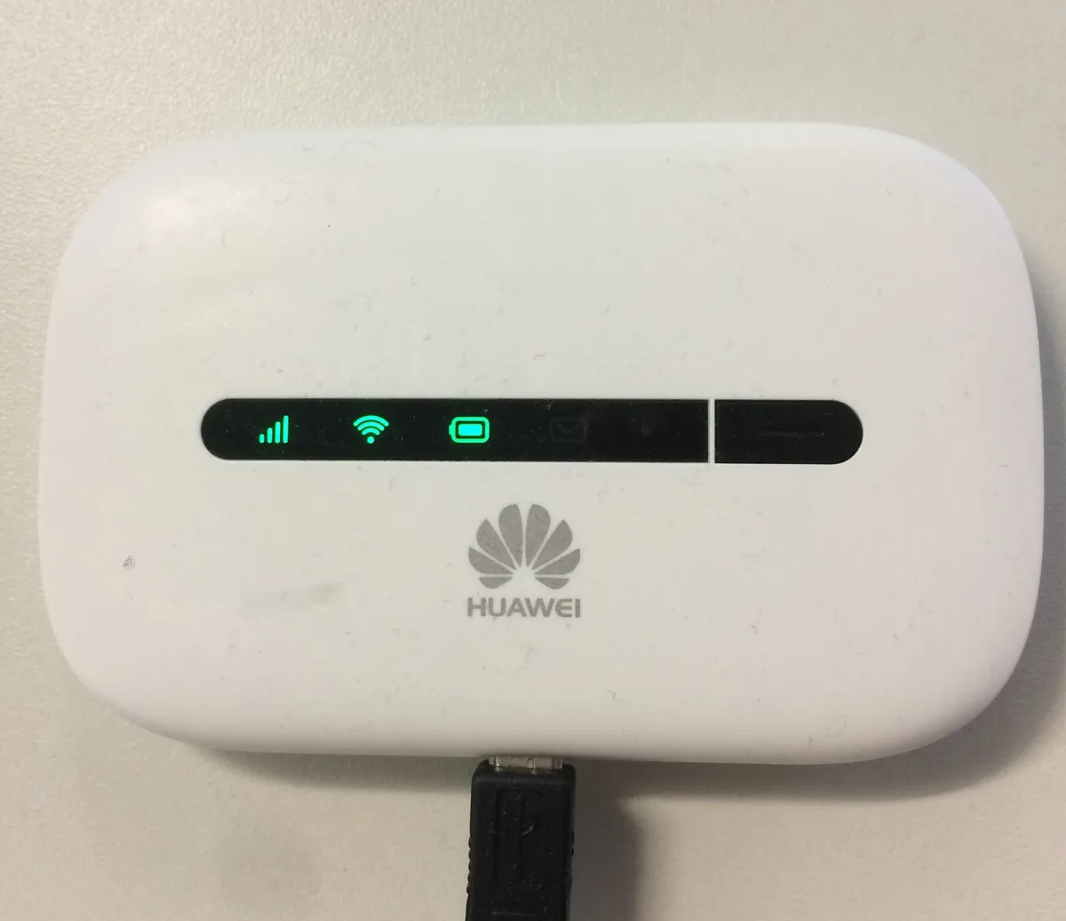 White Huawei portable hotspot on fabric with illuminated signal, Wi-Fi and battery indicators and an attached cable.