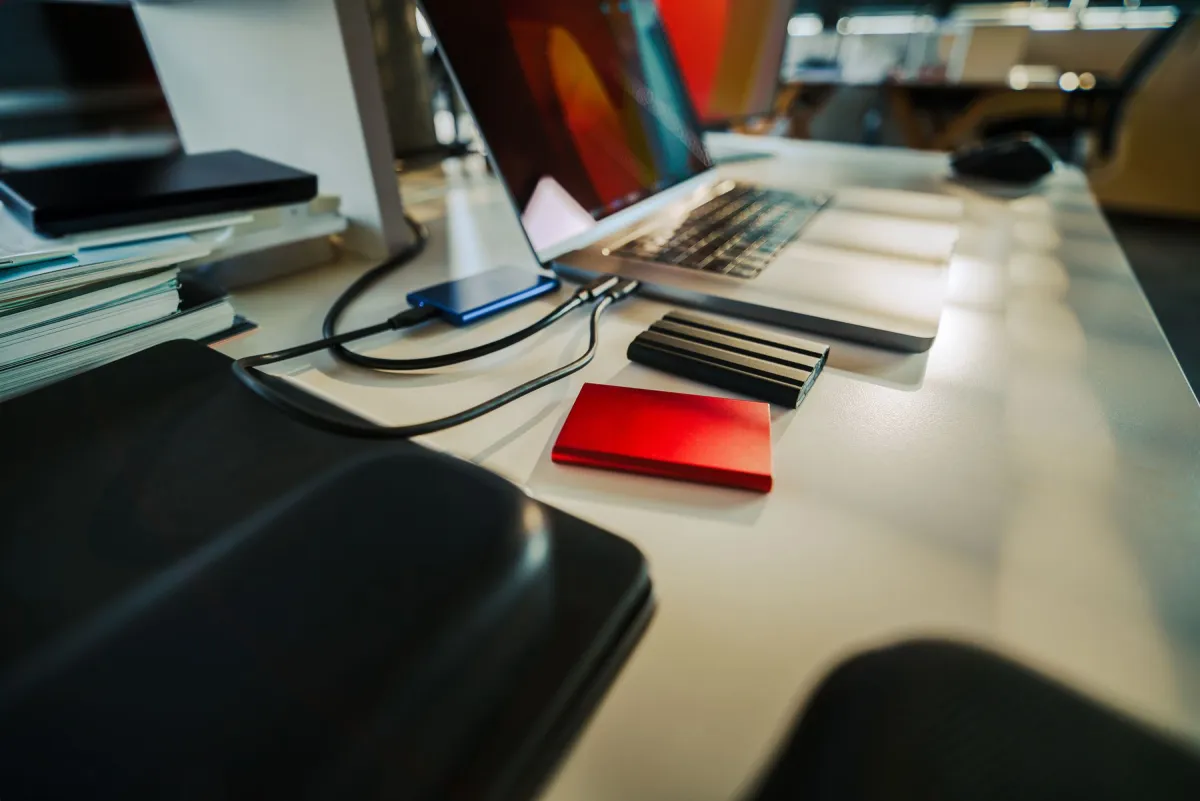Real photograph of a laptop with several external storage devices and cables on a desk.