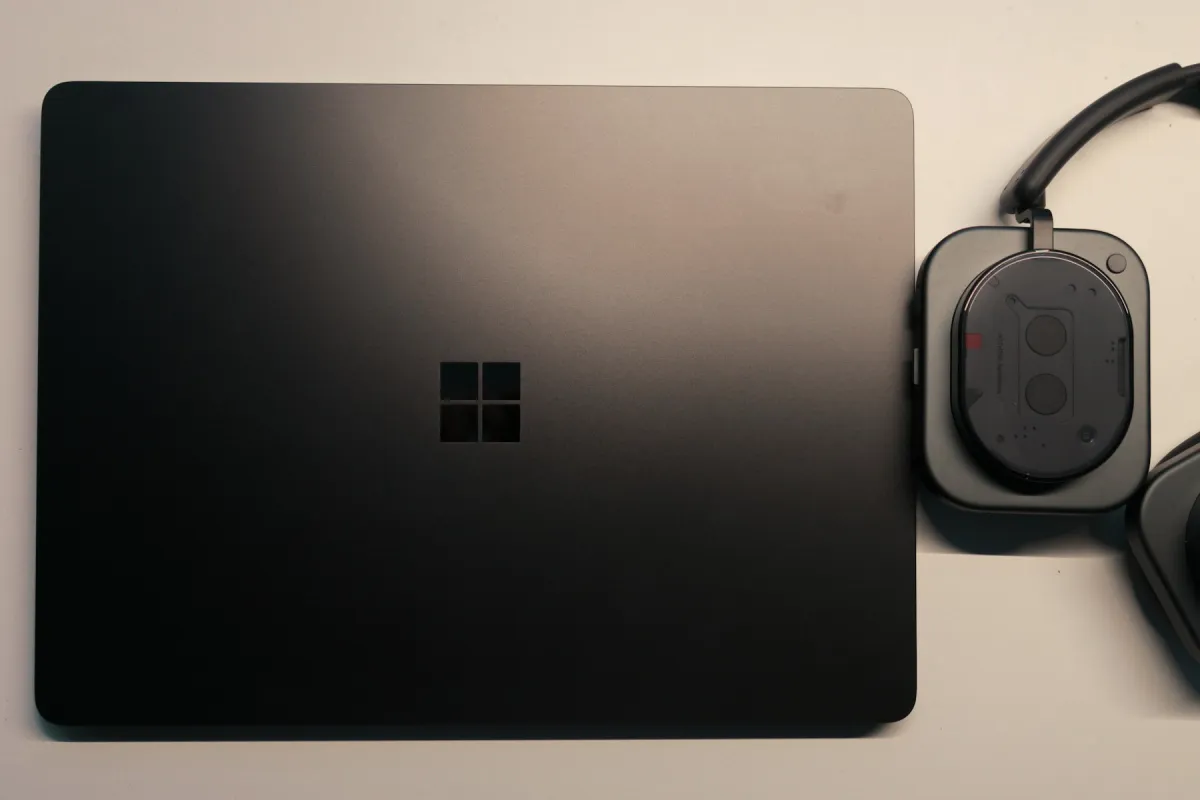 Closed Microsoft Surface laptop beside over-ear headphones on a light tabletop.