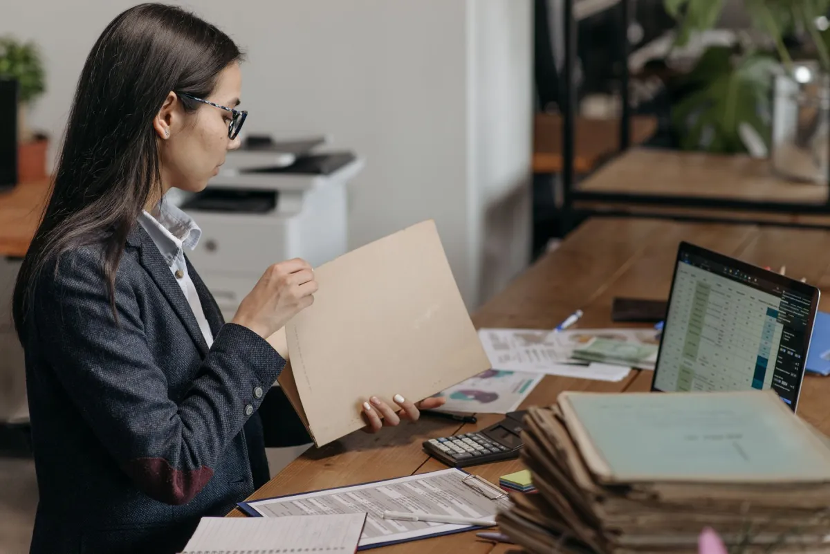 Woman reviewing a paper folder beside a laptop and office files