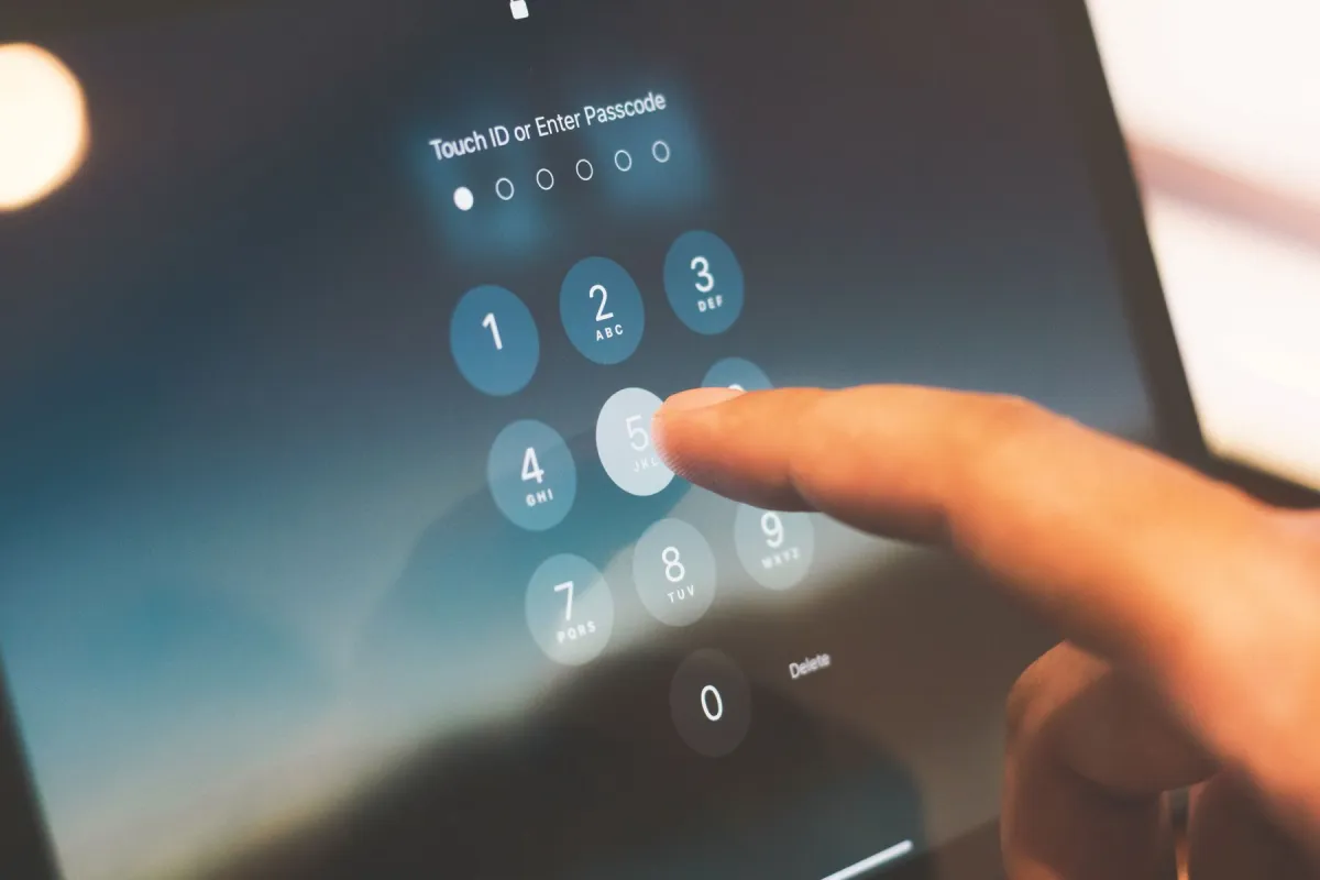 A finger touching the passcode keypad on a handheld device.