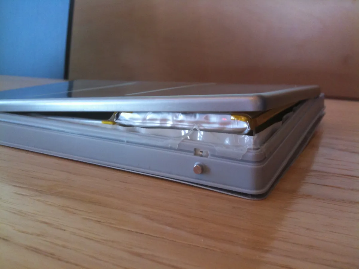 Side view of an older MacBook Pro battery assembly split open around an expanded silver pouch cell.