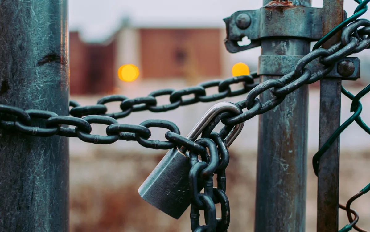 A metal padlock securing heavy chains between two weathered gate posts.