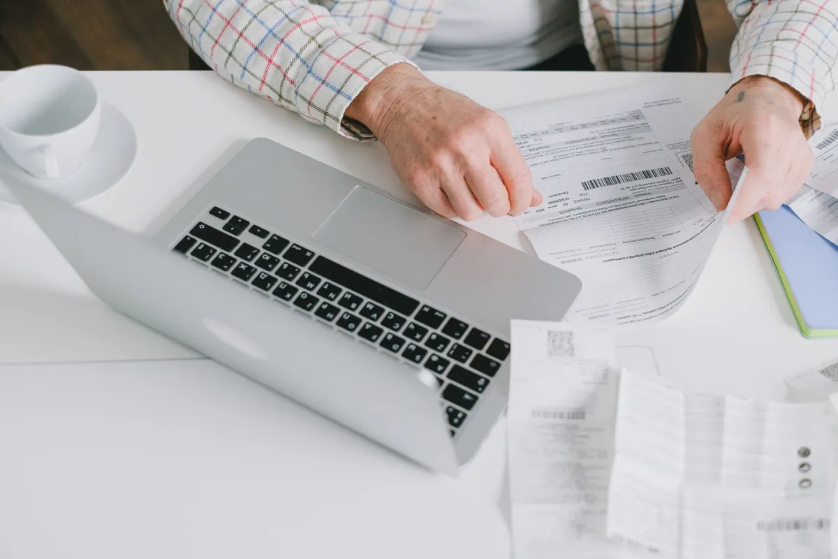 Hands reviewing printed documents beside an open laptop.