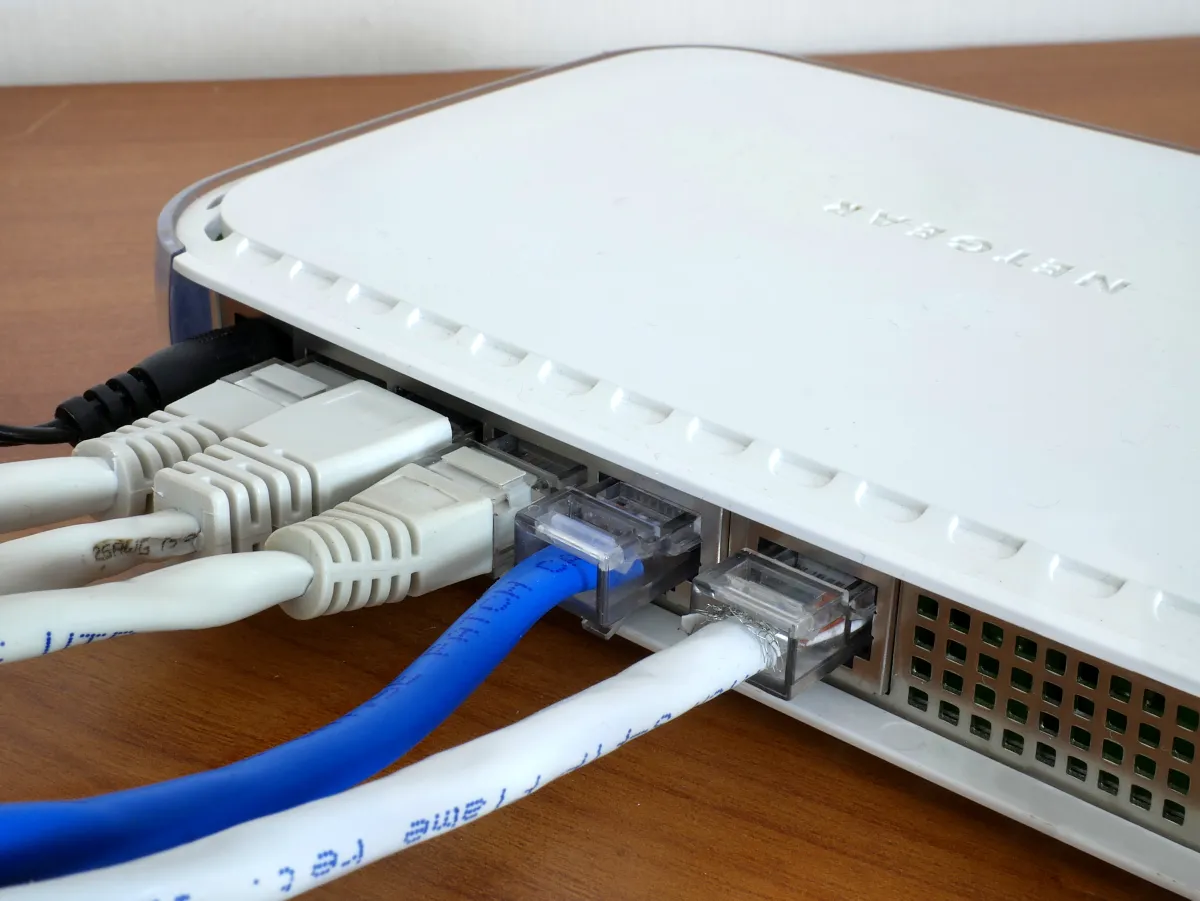 Close-up of white and blue Ethernet cables plugged into the back of a white Netgear router on a wooden surface.