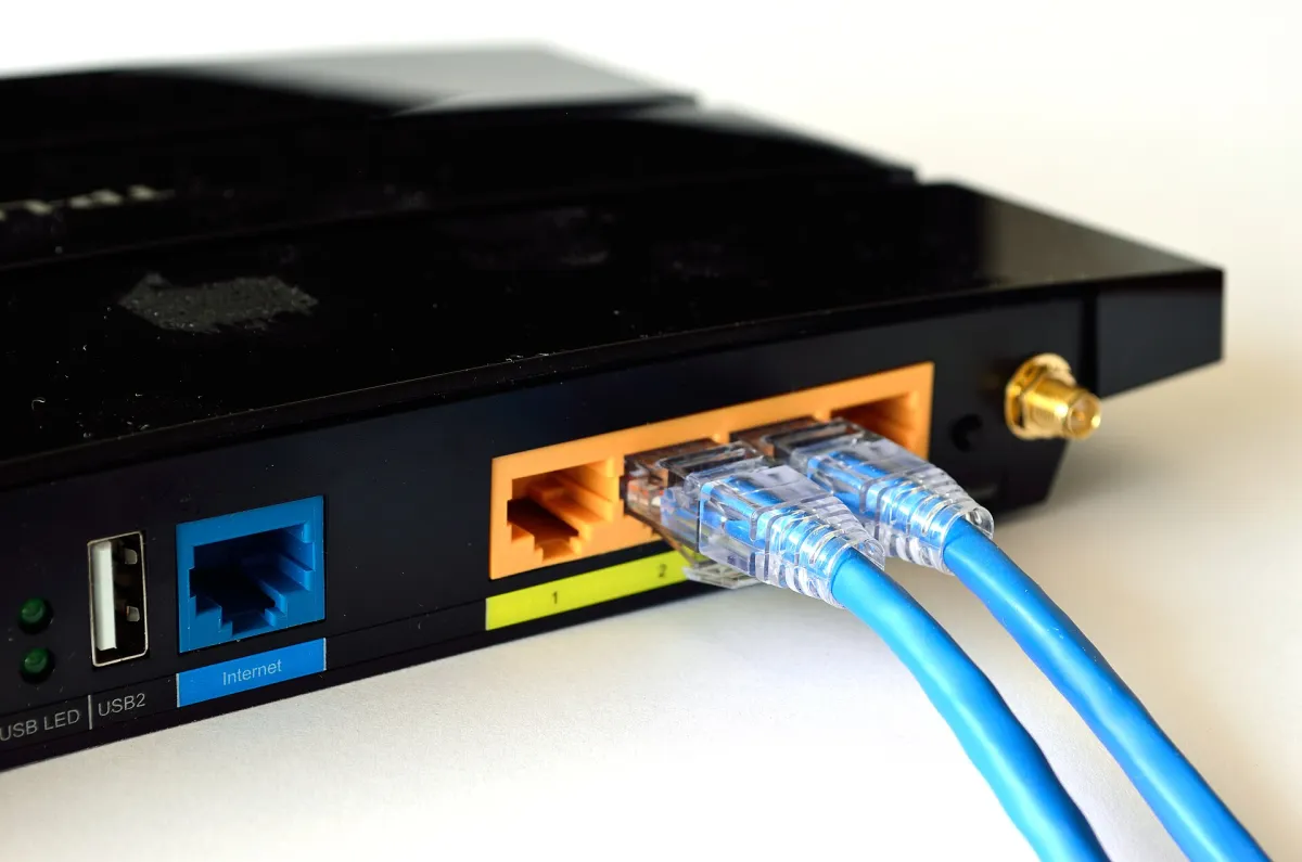 Real close-up of a black home router with two blue Ethernet cables connected to yellow numbered ports and an empty blue port labelled Internet.
