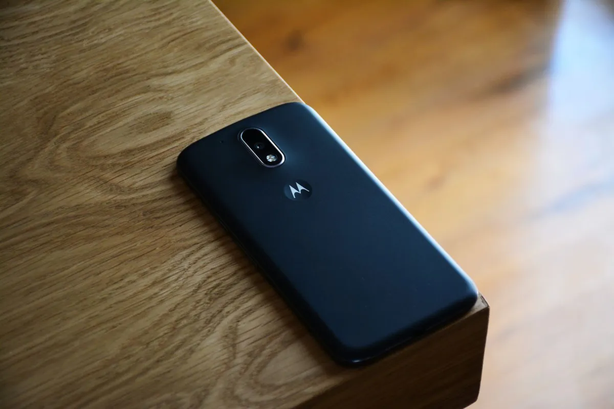 Back of a black Motorola smartphone resting near the edge of a wooden table in natural light.
