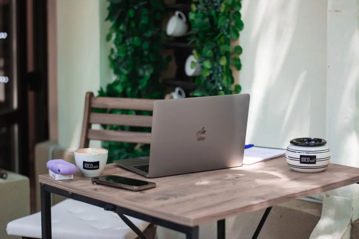 Open laptop, smartphone, coffee cup and notebook on a wooden café table.