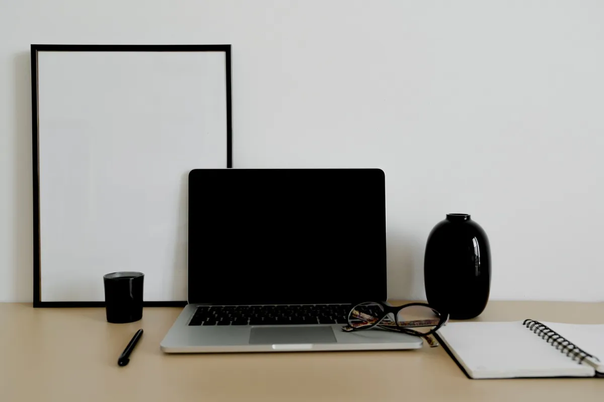 Laptop with a dark screen beside eyeglasses and an open spiral notebook on a tidy desk.