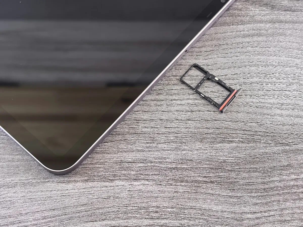 A mobile device with its black SIM tray removed on a grey textured surface.