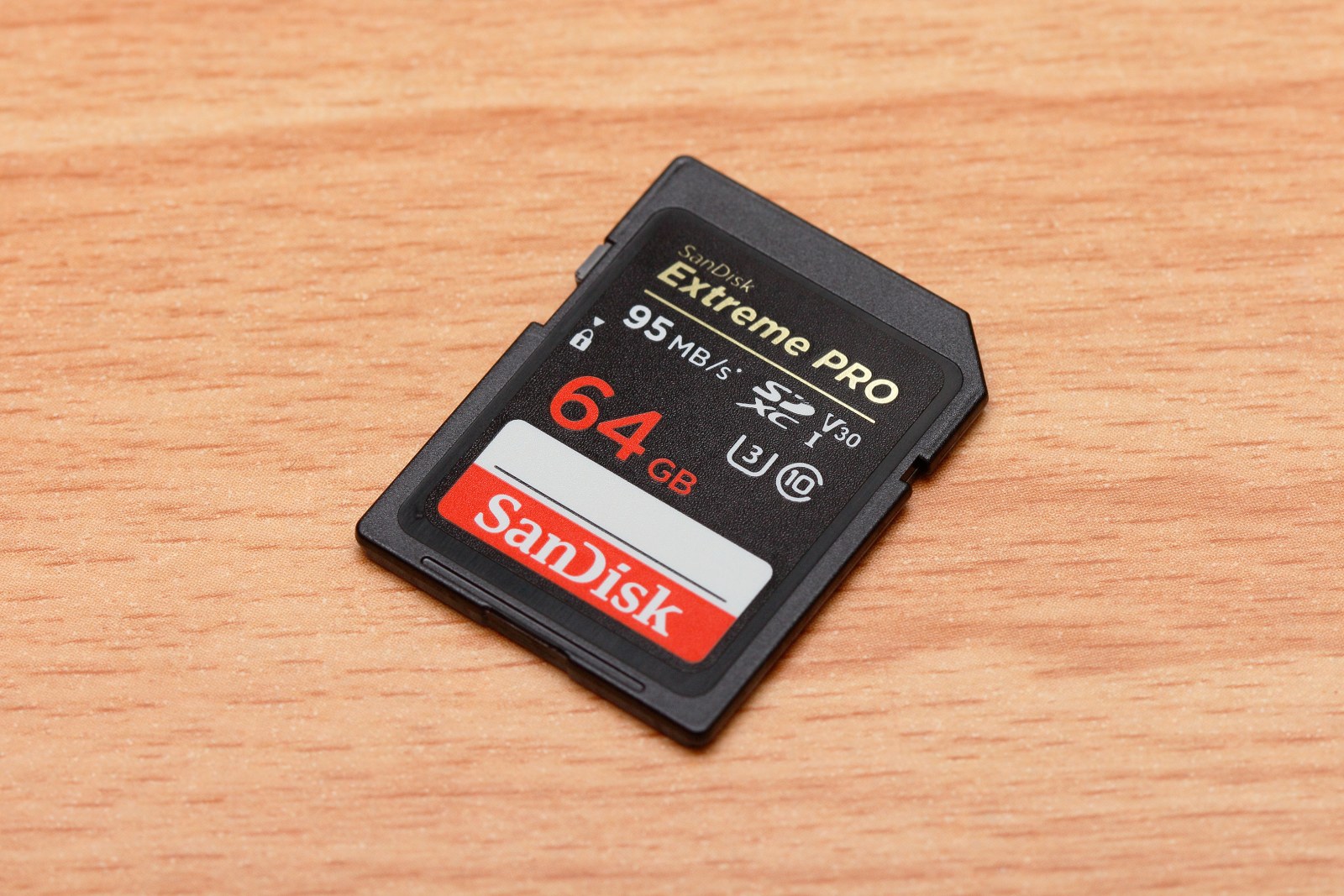 A SanDisk Extreme PRO 64 GB SDXC card on wood, with 95 MB/s, V30, Roman I, U3 and C10 markings clearly visible.